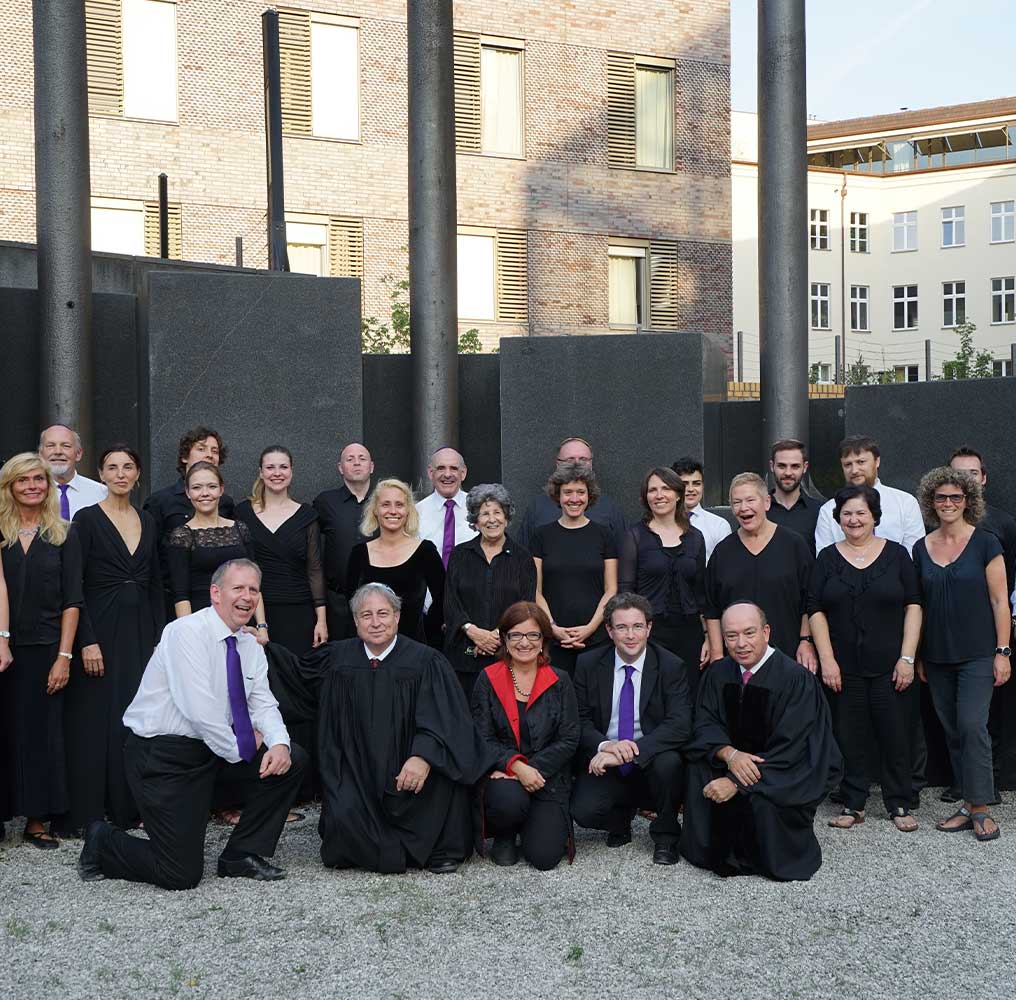 Der Synagogenchor, größtenteils in schwarz gekleidet, einige in weißen Hemden mit lila-blauen Krawatten, steht auf dem Hinterhof der Neuen Synagoge und posiert für ein Gruppenbild.